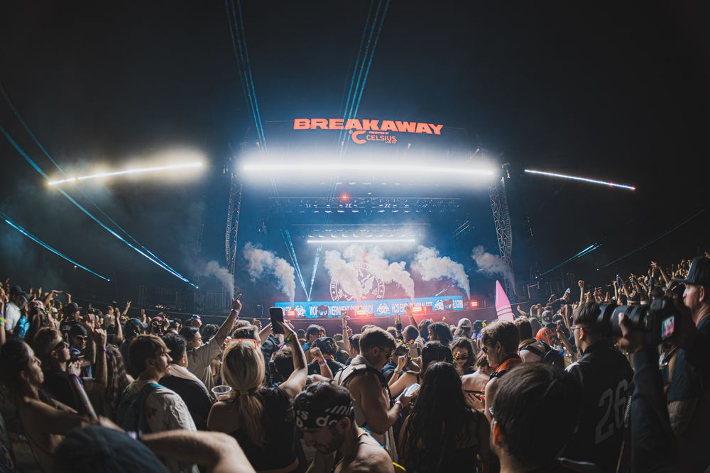 Crowd at Breakaway Music Festival enjoying a vibrant night show with colorful stage lights and laser beams.