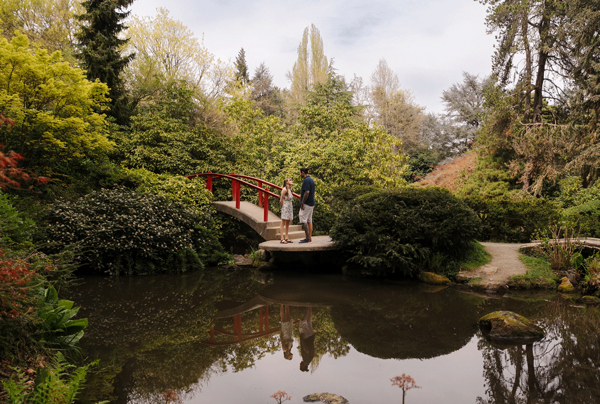 Couple embracing outdoors, woman in floral dress with tattoos, man with sleeve tattoo, sharing a romantic moment.