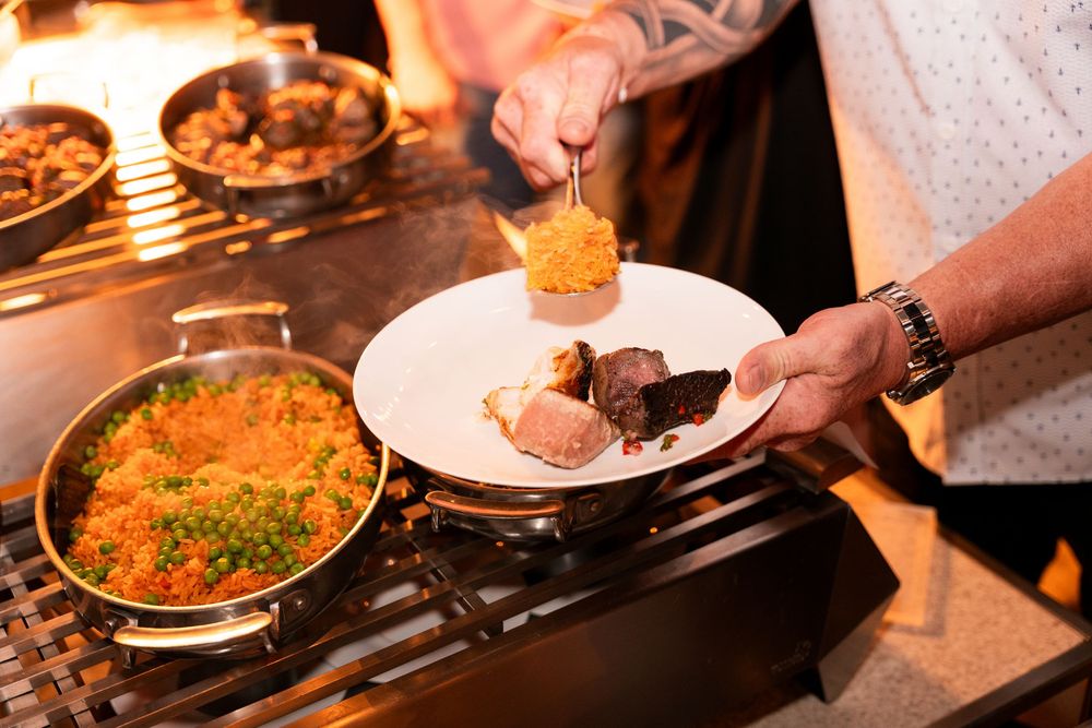 Chef plating a gourmet dish with rice and vegetables on a white plate over a stovetop in a restaurant kitchen.