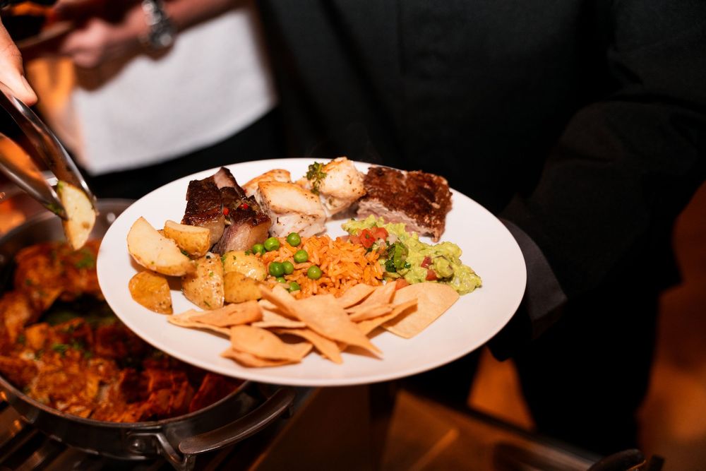 A plate of food with meat, rice, vegetables, and chips served at a buffet event.