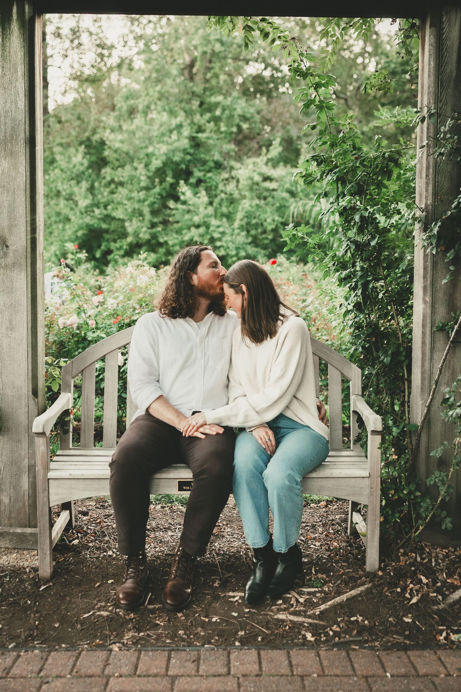 Couple embracing on a wooden bench during Bon Air Rose Garden proposal session