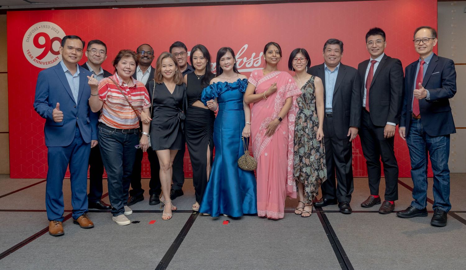 A group of formally dressed people pose together at a corporate event with red background.