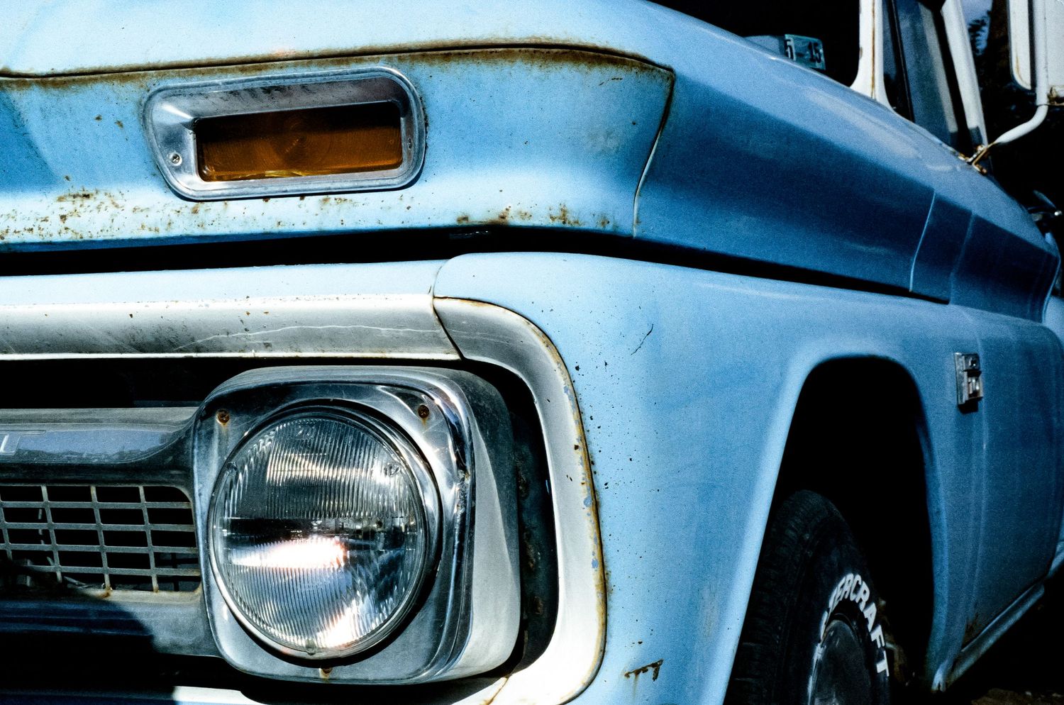 Close-up of a vintage blue truck's front headlight and chrome grille section.
