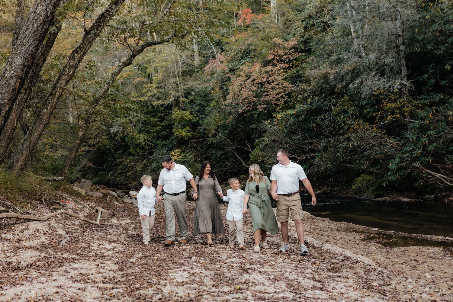 A family walks together along a scenic wooded creek during an autumn photo session.