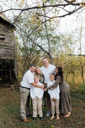 A family shares joyful laughter together during an autumn outdoor photoshoot near rustic buildings.