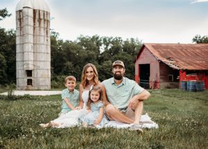 A rustic farm setting with a tall silo and red barn in the background surrounded by green grass.