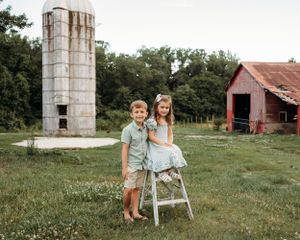 A pastoral scene with a tall concrete silo and red barn in the background on a sunny day.