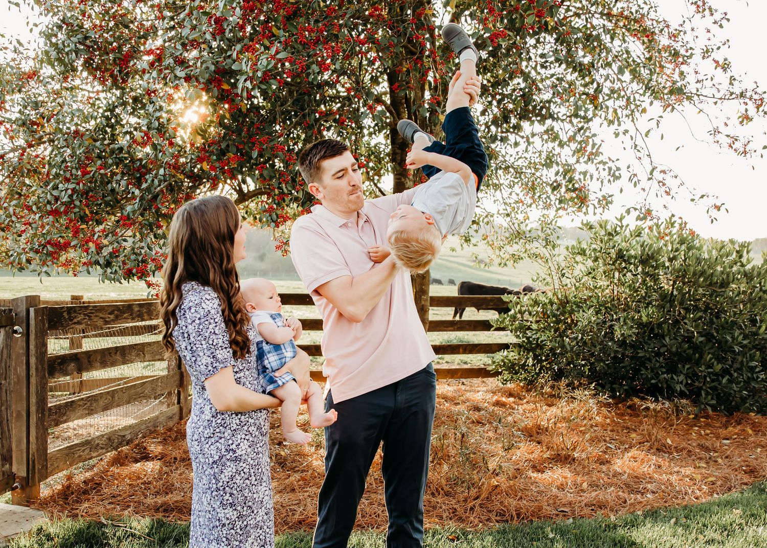 Family members interact playfully beneath autumn trees with red berries.