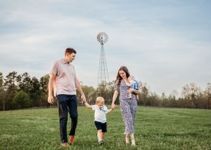 Family plays together in a grassy field at sunset with a windmill in the background.