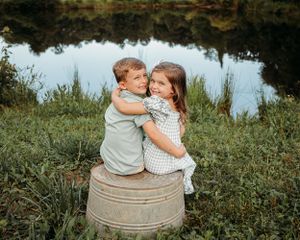 Children sitting together on a metal barrel in a grassy field with natural lighting.