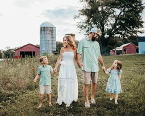 Family members in coordinating mint green and white outfits walking through a grassy field near a silo.