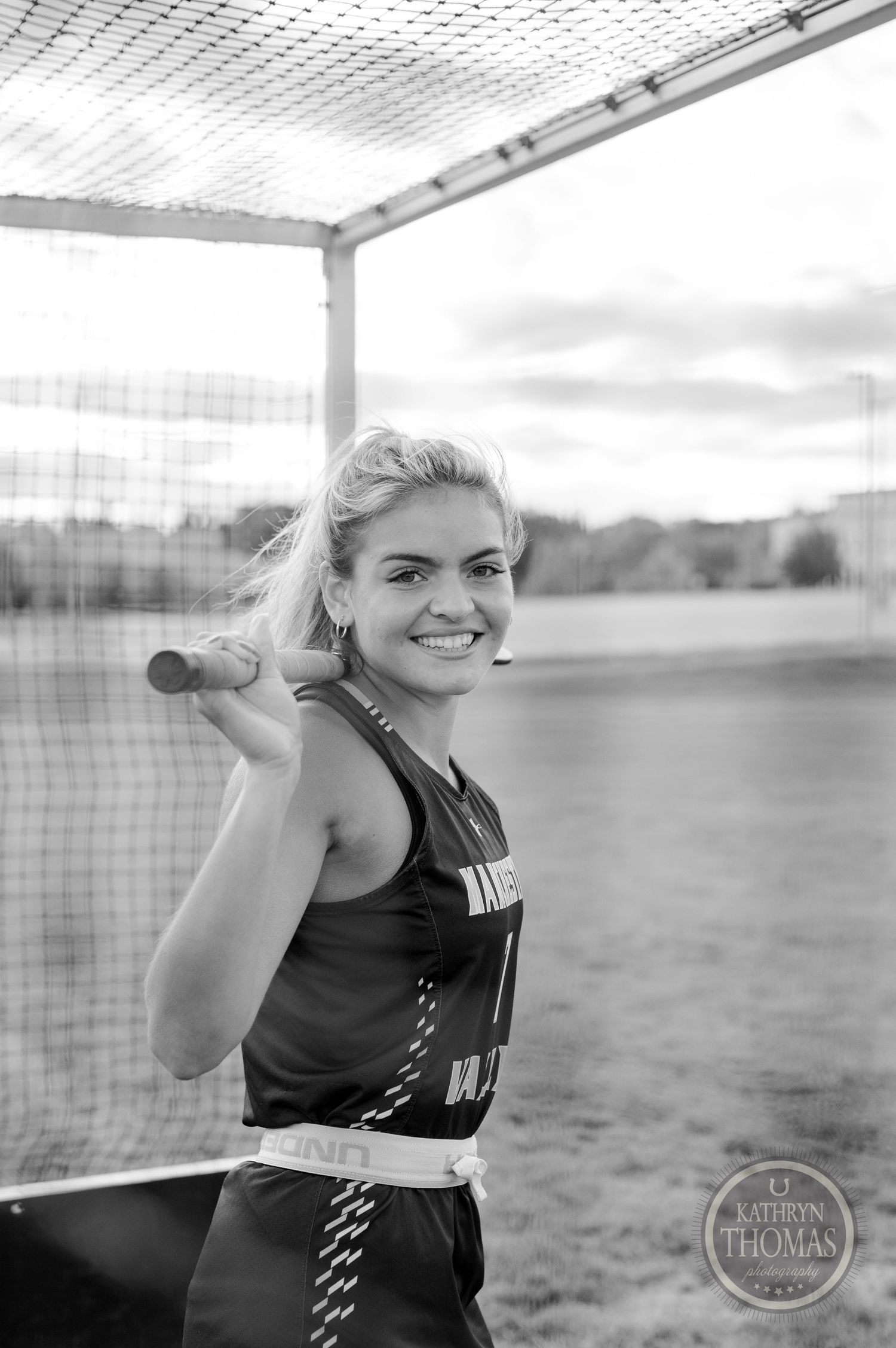 Black and white photo of athlete holding field hockey stick under goal net.