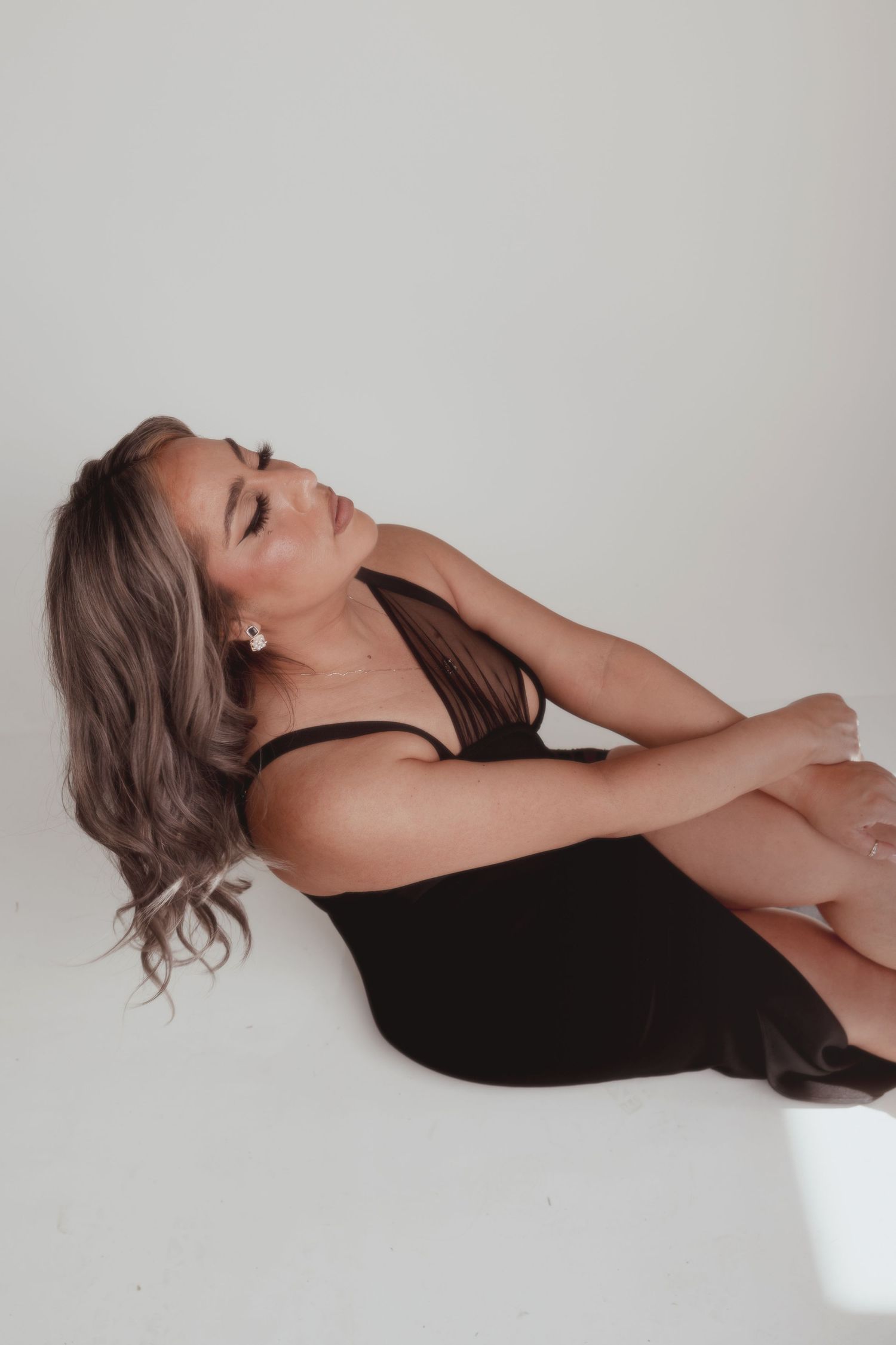 Artistic portrait of woman in black outfit posing against white backdrop.