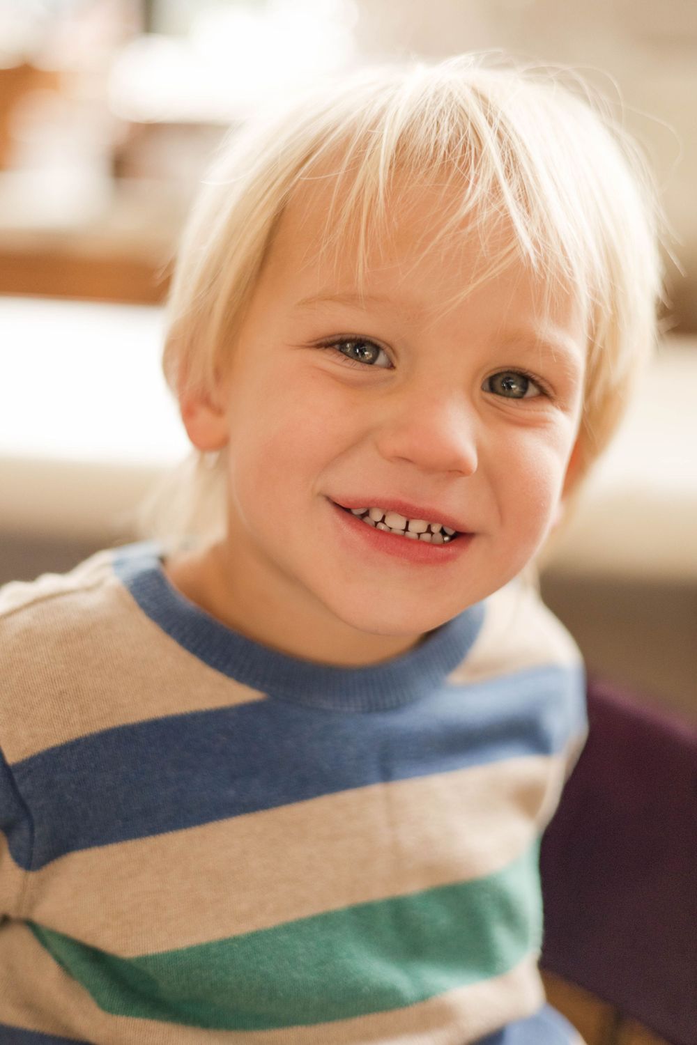 A child wearing a striped sweater smiles at the camera in a warm indoor setting.