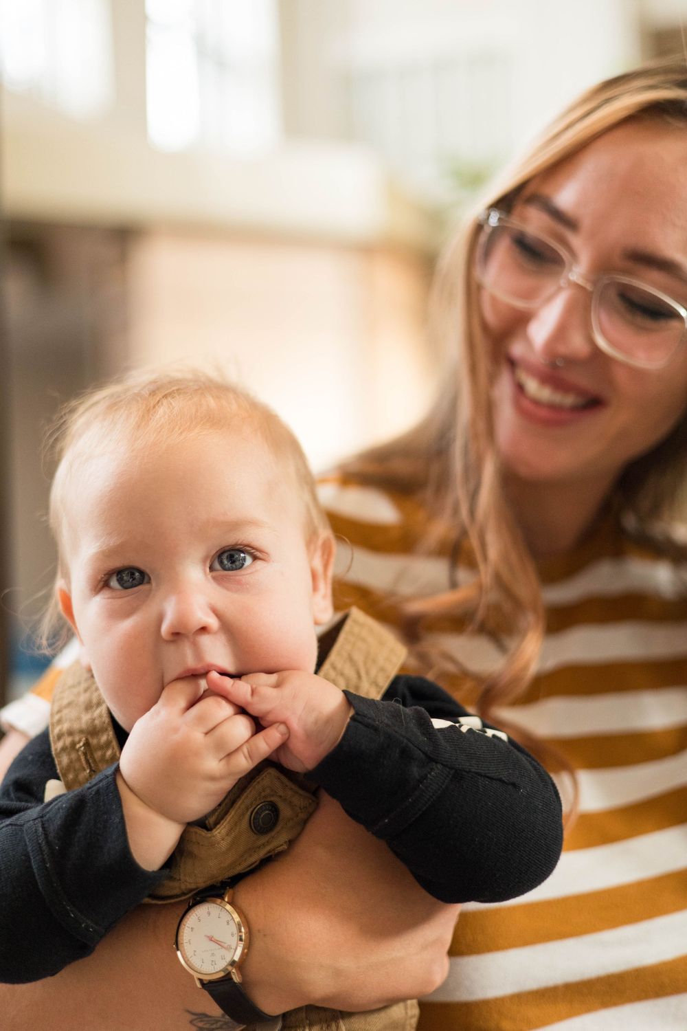 A baby in black clothing is held while being photographed indoors.