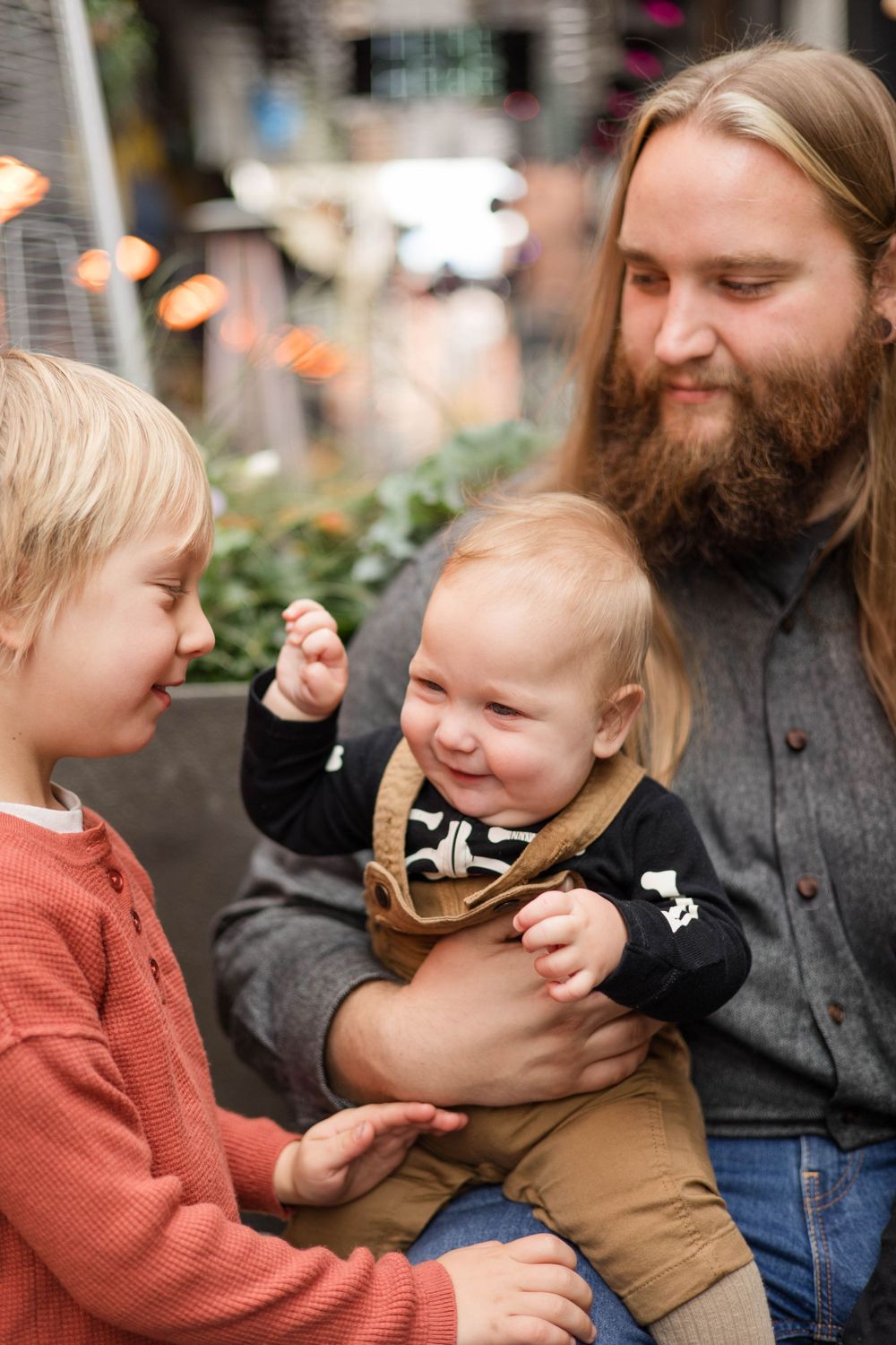 A joyful family moment captured outdoors with a baby in overalls sharing laughs and smiles.