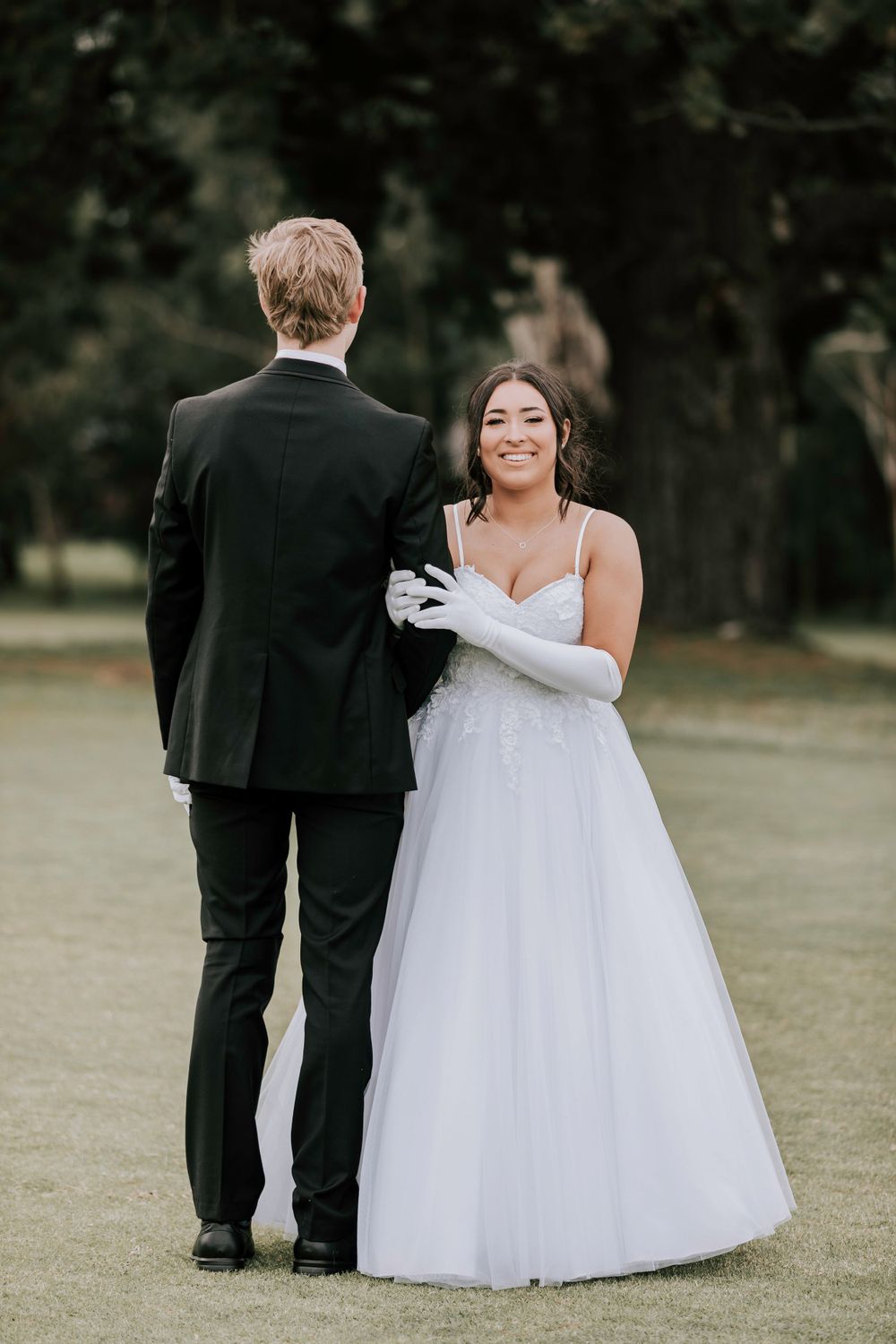 Bride in white gown and groom in black suit exchange vows on a golf course.