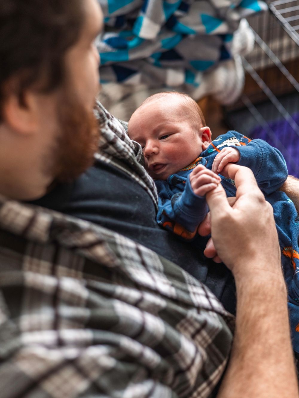 Parent in plaid shirt cradles newborn baby wearing blue outfit.