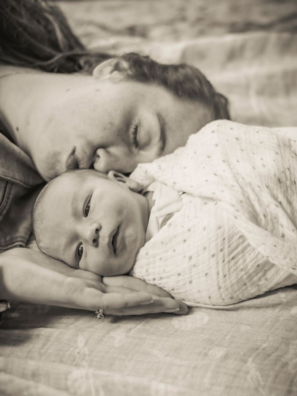 Intimate black and white portrait of parent and baby lying close together on soft bedding.