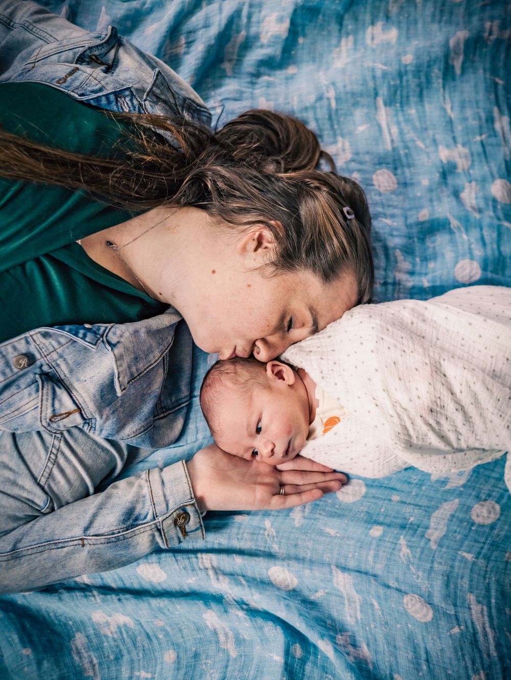Intimate portrait of parent and baby lying on blue textured bedding sharing a tender moment.