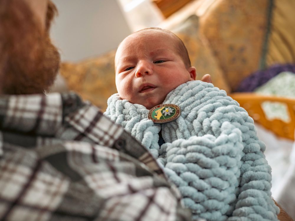 Newborn baby wearing blue sweater being held by adult in plaid shirt.