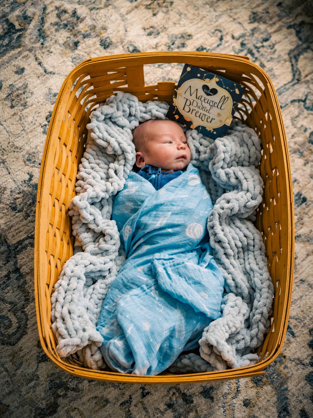 Peaceful baby in blue swaddle sleeping in wooden basket on textured blanket.