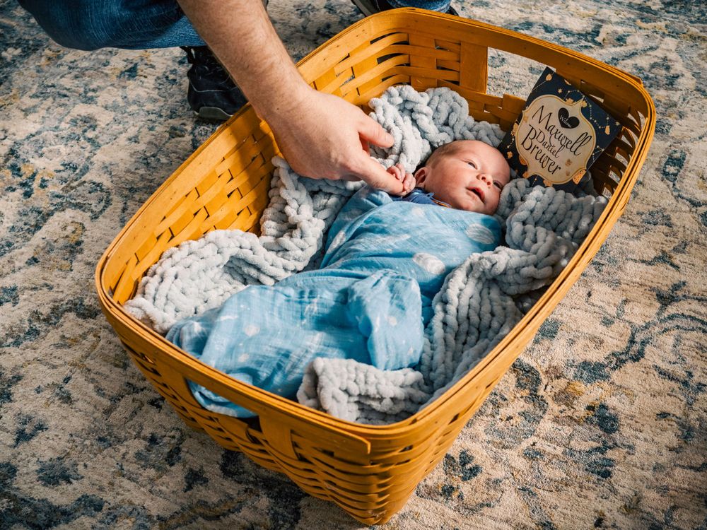 Baby wearing blue sleepwear rests in a woven basket on a patterned rug.