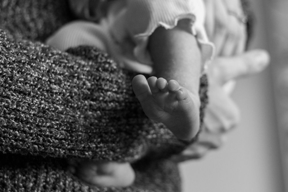 Black and white close-up of tiny baby feet being held in sweater-clad hands.
