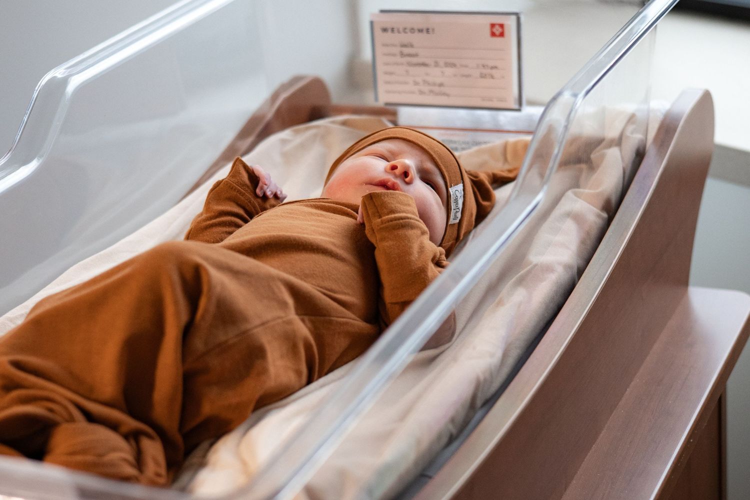 Baby lays in hospital bassinet with a orange knotted gown and hat