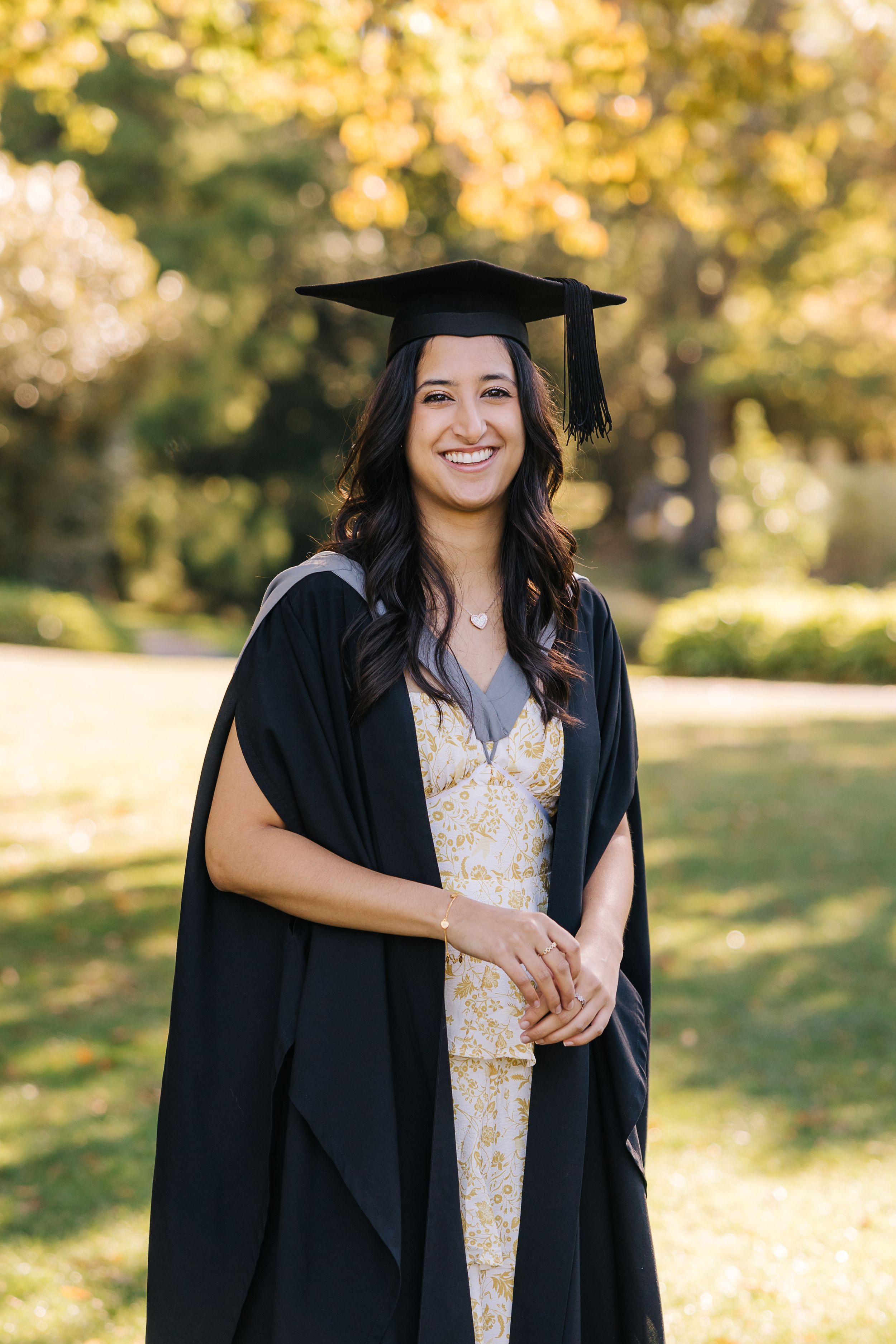 Young woman wearing a cap and gown for her graduation with autumn trees in the background at the Christchurch Botanic gardens.