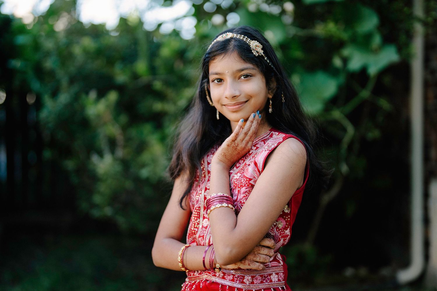 A person in a red floral dress poses outdoors against a green foliage background.
