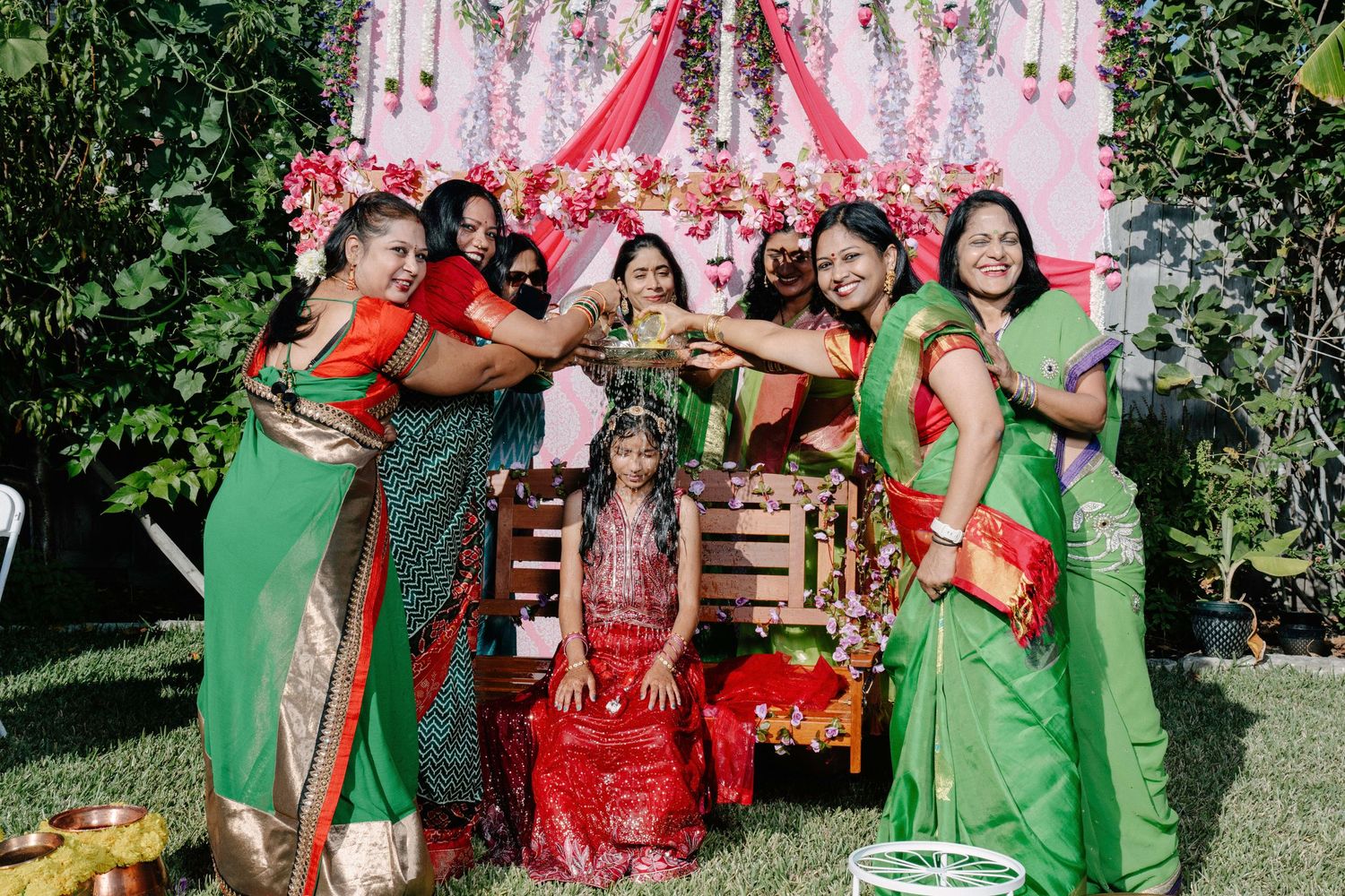 Wedding party in green dresses and red attire celebrating outdoors with confetti and joyful expressions.