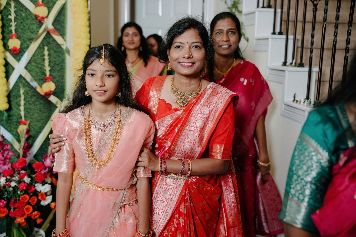 Indoor celebration with guests wearing traditional South Asian attire in pink, red, and green colors.