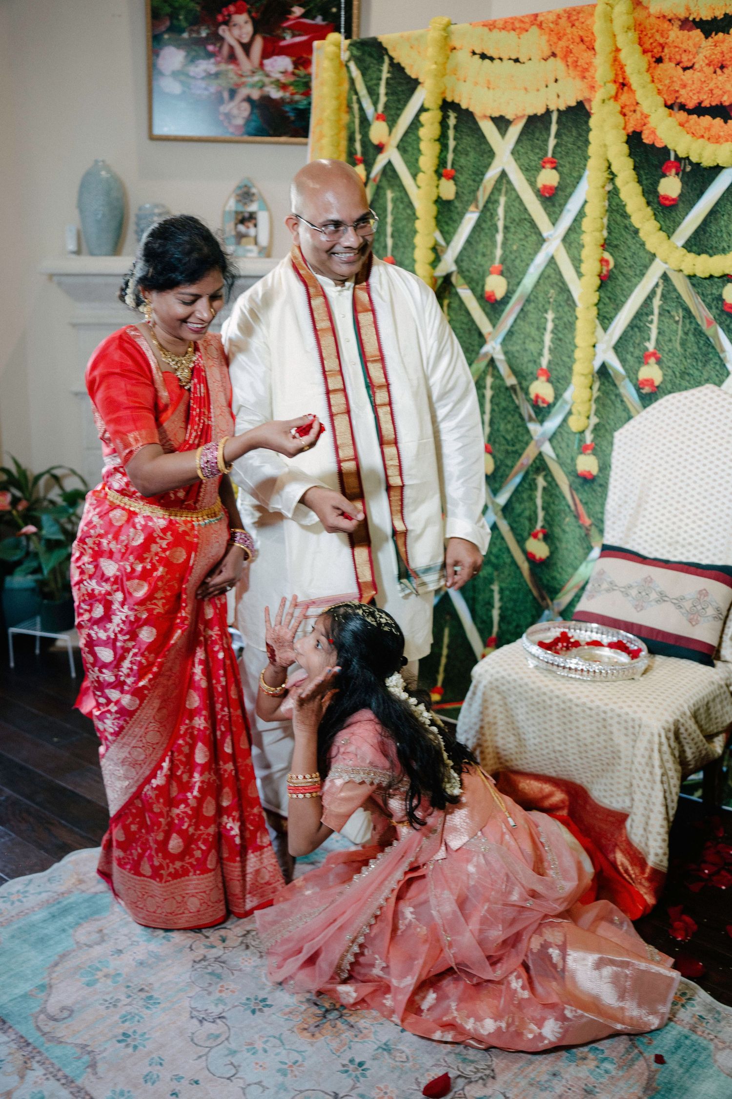 Traditional wedding ceremony with couple seated on floor wearing red and white attire during ritual celebrations.