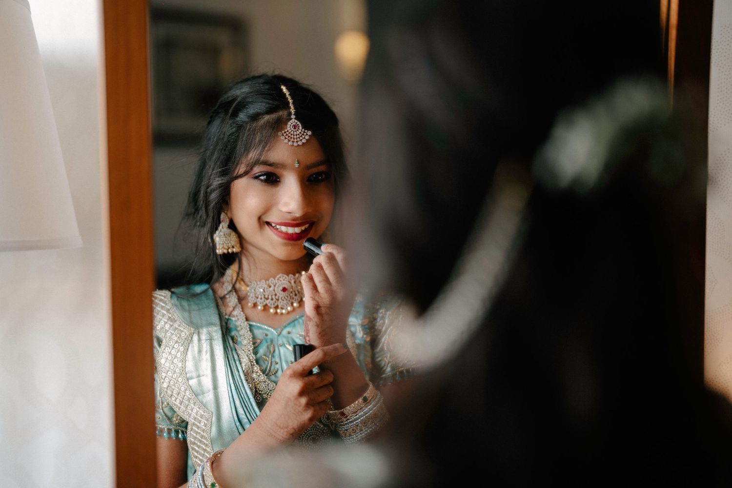 A person in traditional Indian attire and jewelry getting ready in soft window lighting.