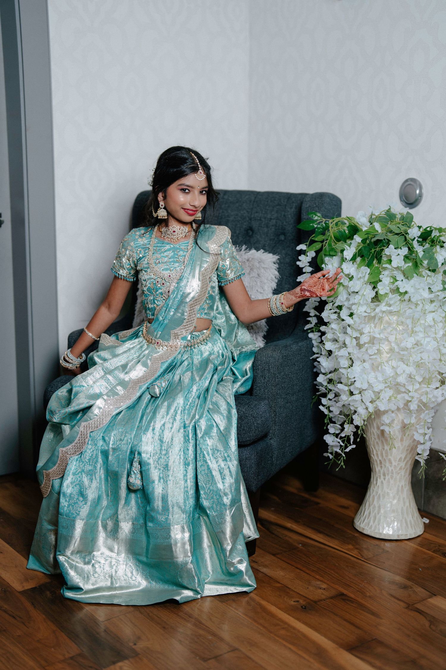 A series of photos showing someone in a turquoise princess gown posing playfully on a gray couch with white floral decorations.