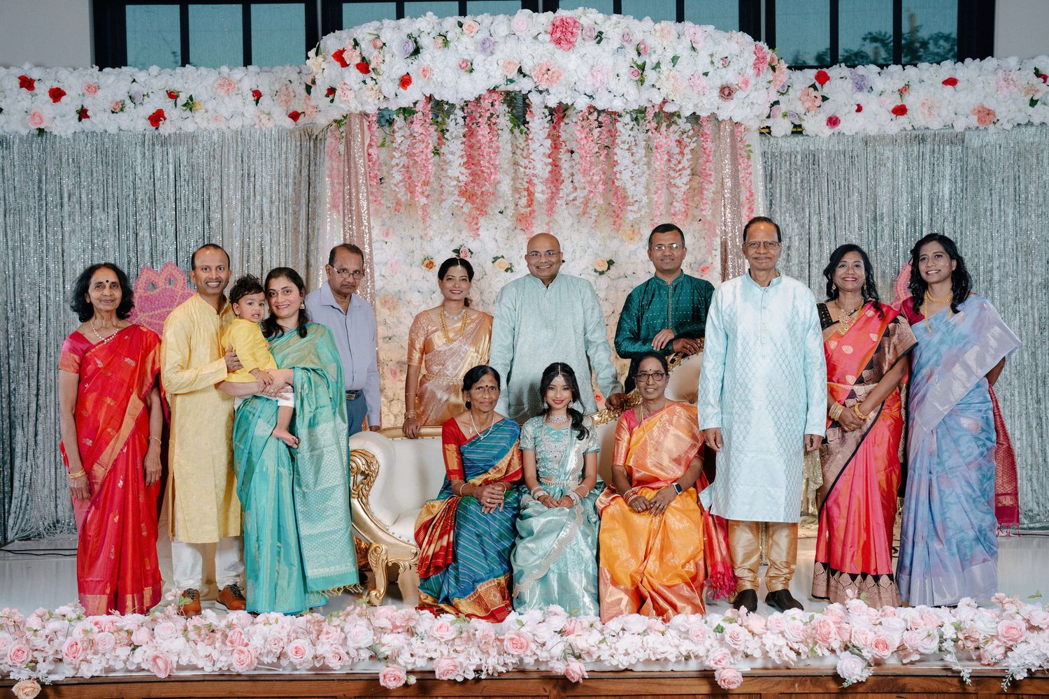 A group of people in traditional Indian attire including saris and kurtas pose together for a formal event photo.