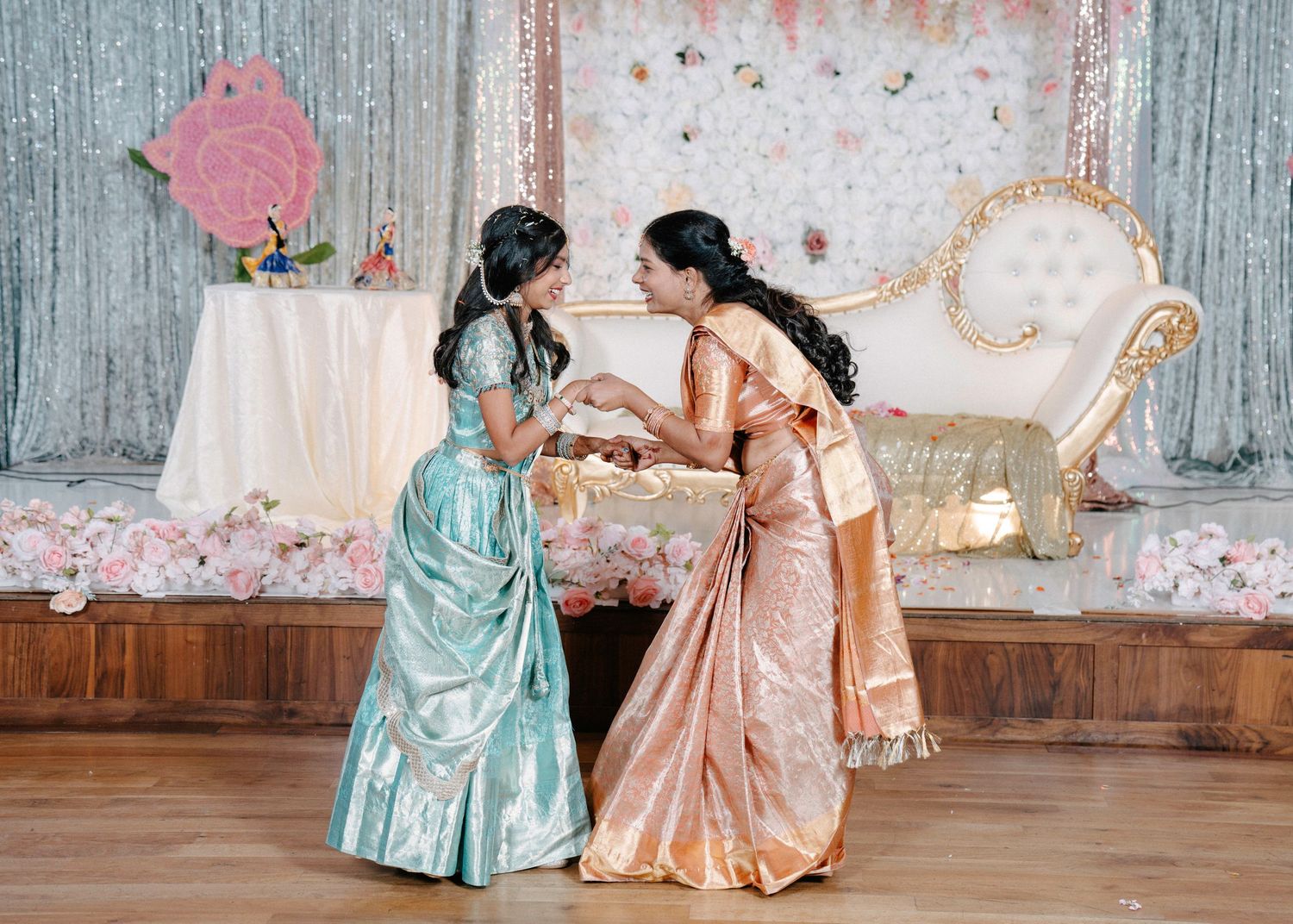 Two people in elegant gowns share a tender moment during a dance on a rustic wooden floor.