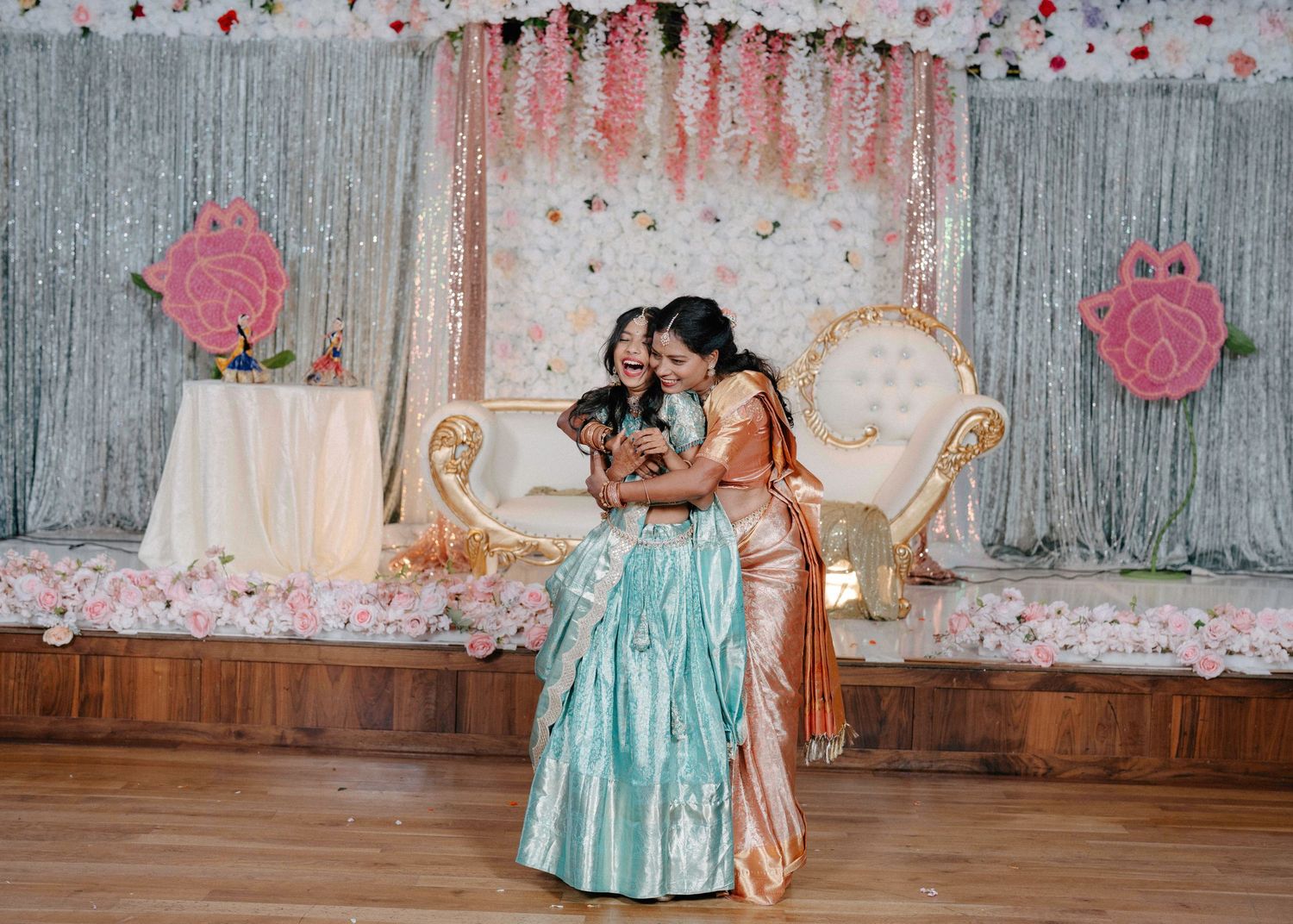 A couple shares an intimate dance moment on a decorated stage with silver backdrop and pink floral accents.