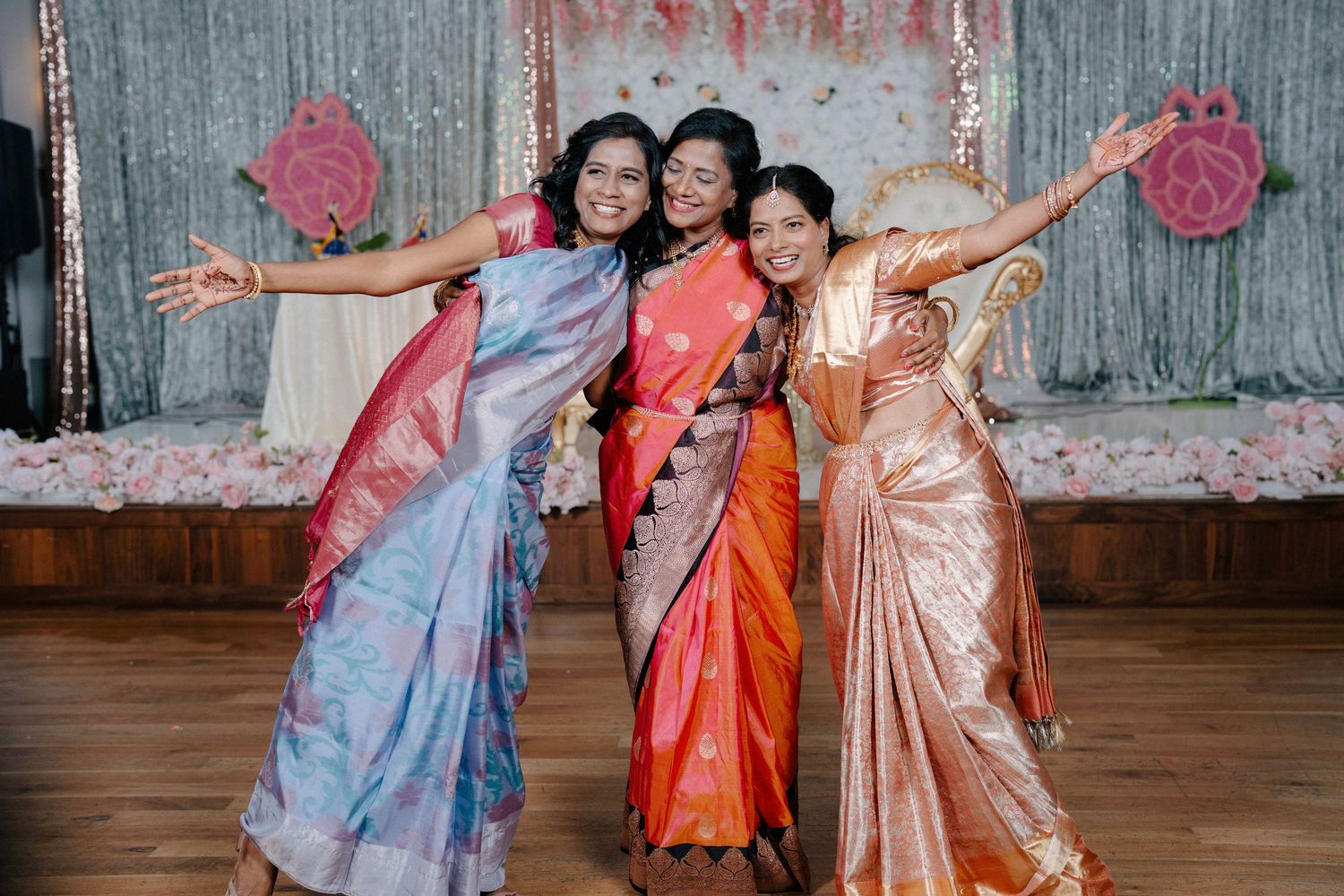 Three friends in colorful traditional outfits posing joyfully together in a studio setting.