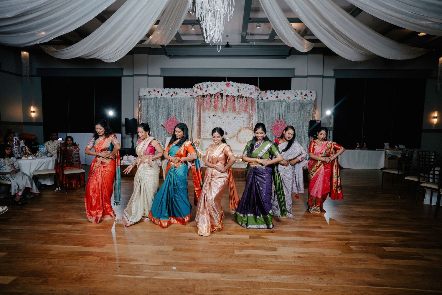 A wide panoramic shot of guests seated in formal attire at an elegant indoor event venue with draped white ceiling decor.