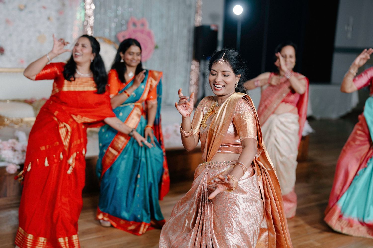 People dance and celebrate at a vibrant Indian wedding reception with colorful traditional outfits and festive decor.