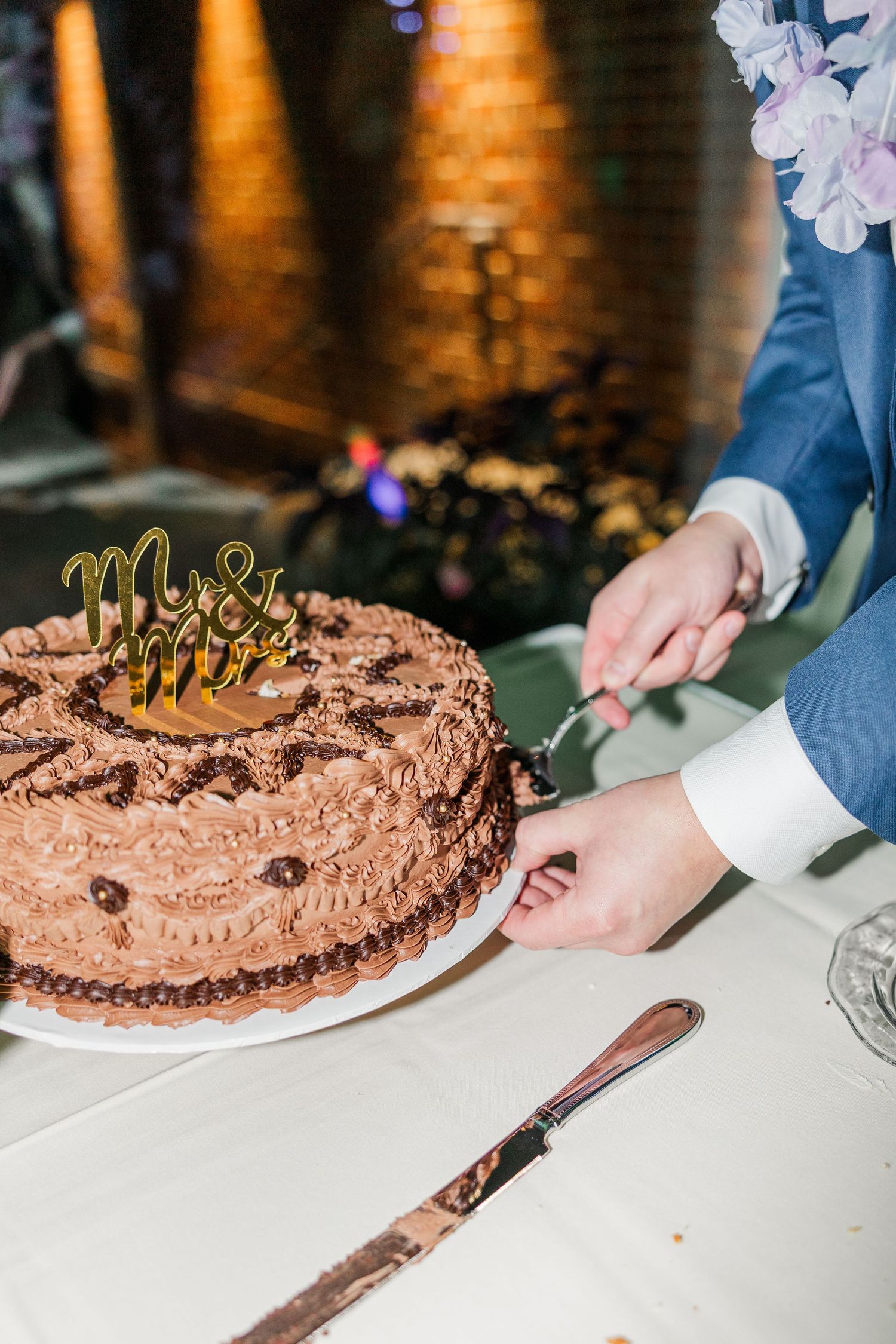 Chocolate groom's cake being cut into slices at a wedding reception with a silver serving knife.