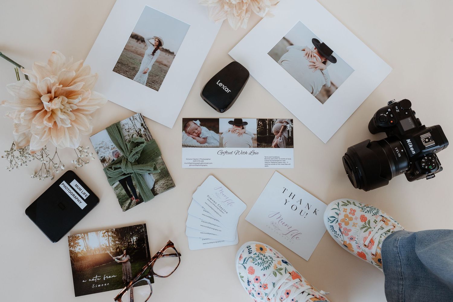 A flatlay arrangement of photography equipment, cameras, and printed photos scattered on a light beige surface.