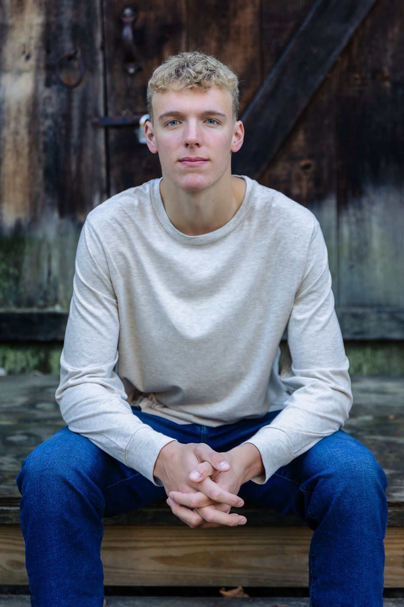 Man sits on steps against rustic cabin in high school senior photos taken at Parker Mill County Park in Ann Arbor.