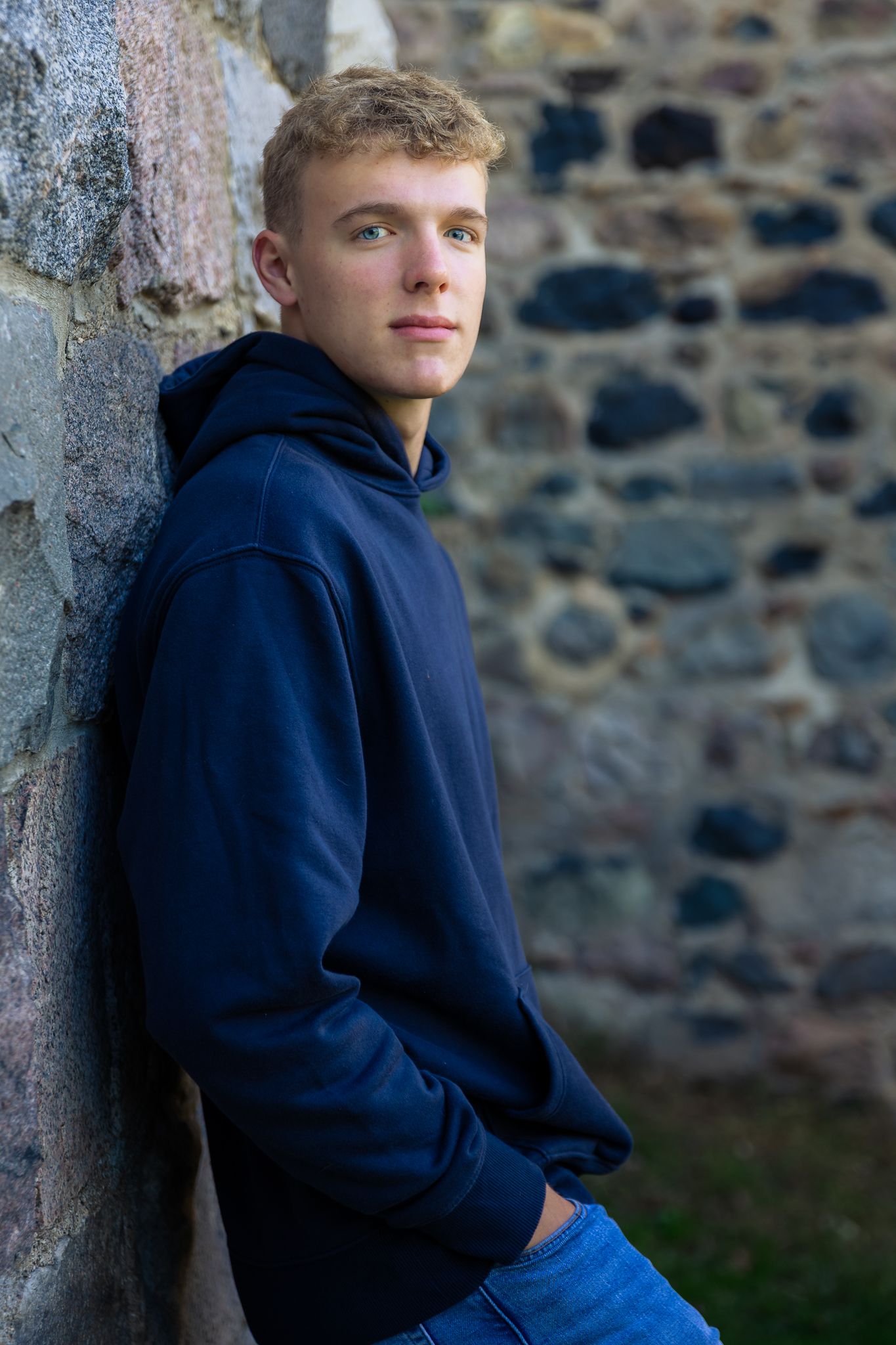 Man leans against stone wall for high school senior photos at Parker Mill County Park in Ann Arbor.
