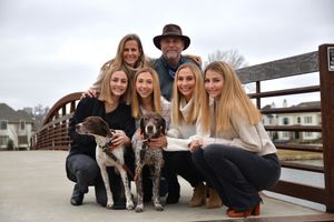 Family of six posing on a bridge with two spotted dogs on a cloudy day.