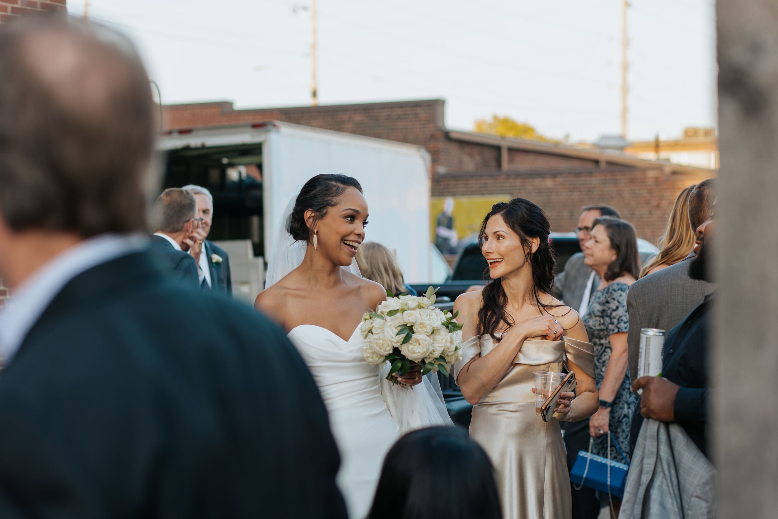 Wedding guests enjoy drinks and laughter during an outdoor cocktail reception at sunset.