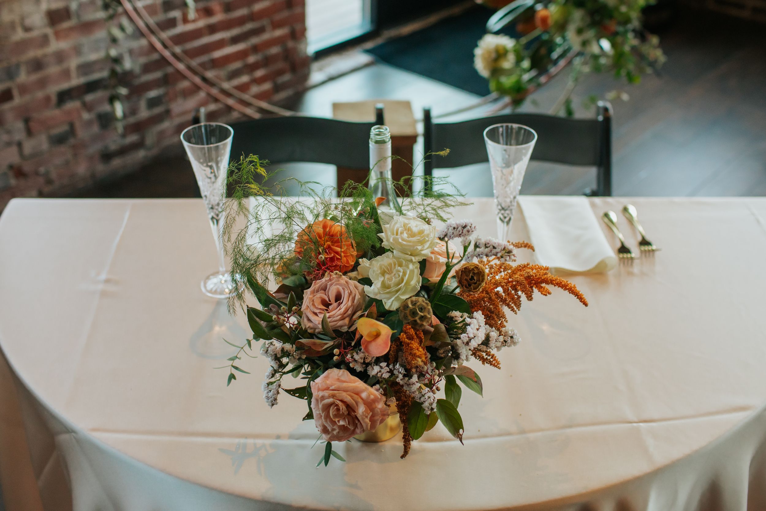 Wedding reception table settings with elegant floral centerpieces, crystal glasses, and soft peach and coral flowers.