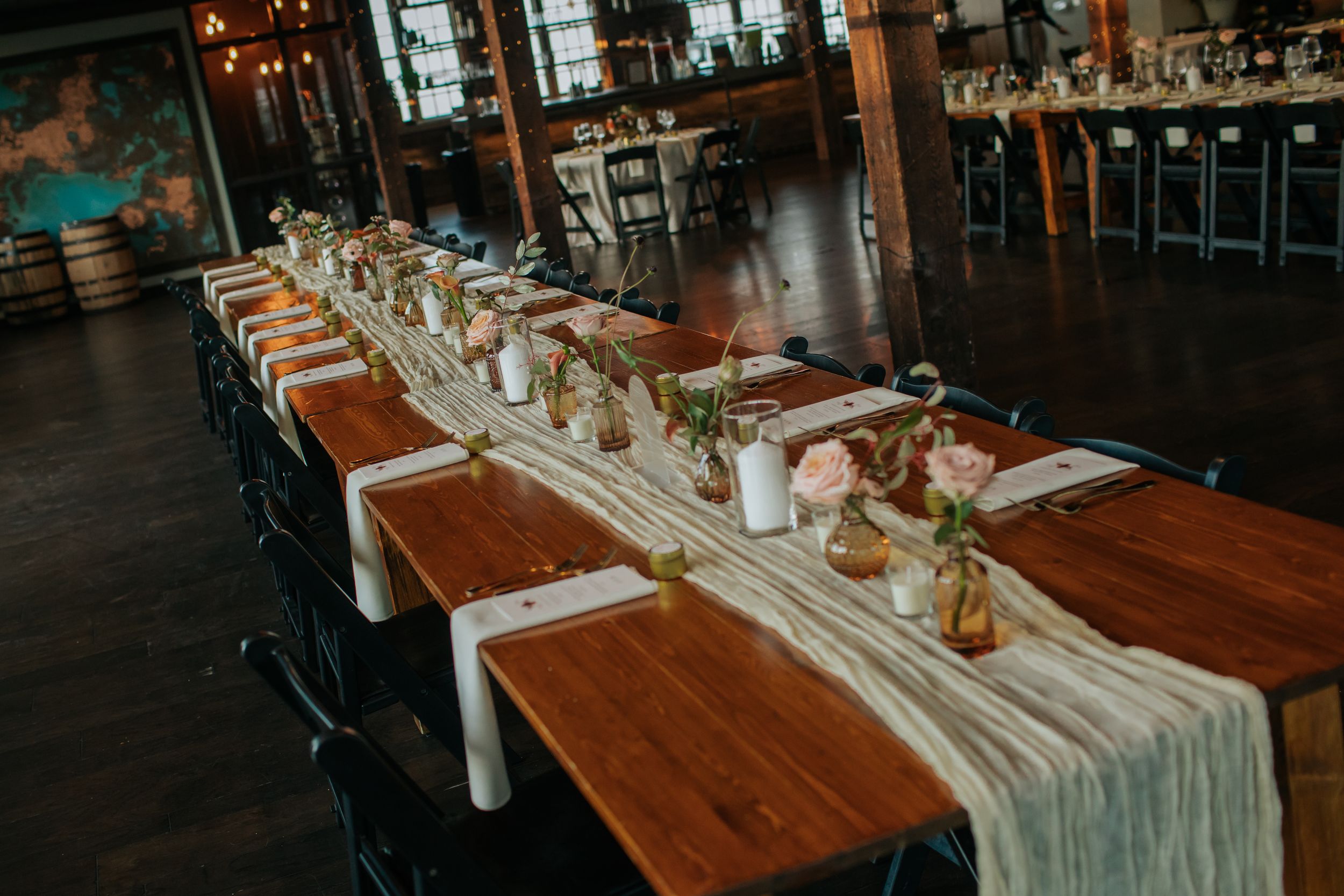 Long wooden dining tables with elegant place settings and glowing candlelight create an intimate restaurant atmosphere.
